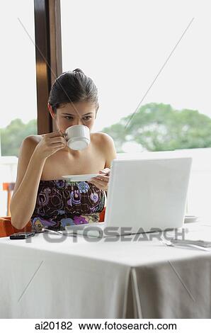 Woman sitting in restaurant, using laptop, drinking from cup View Large Photo Image Stock Image - Woman sitting in restaurant, using laptop, drinking from cup. Fotosearch