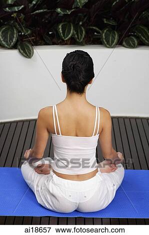 Stock Photo - Woman sitting in yoga position, meditating, rear view. Fotosearch