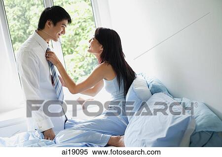 Woman sitting on bed, adjusting man's tie, turning to look at camera View Large Photo Image Stock Photography - Woman sitting on bed, adjusting man's tie, turning to look at camera. Fotosearch