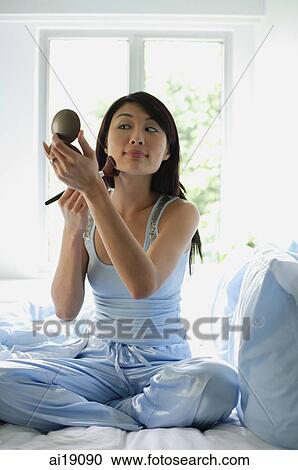 Woman sitting on bed, applying make-up View Large Photo Image Stock Image - Woman sitting on bed, applying make-up. Fotosearch
