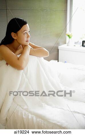 Woman sitting on bed, hugging knees View Large Photo Image Picture - Woman sitting on bed, hugging knees. Fotosearch