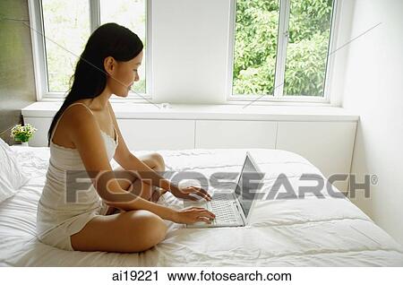Woman sitting on bed, using laptop View Large Photo Image Stock Image - Woman sitting on bed, using laptop. Fotosearch