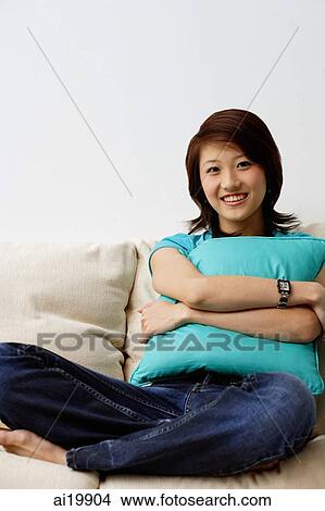 Woman sitting on sofa, hugging cushion, looking at camera View Large Photo Image Picture - Woman sitting on sofa, hugging cushion, looking at camera. Fotosearch