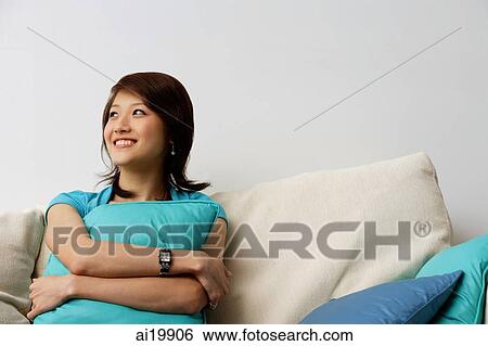 Woman sitting on sofa, hugging cushion, looking away, smiling View Large Photo Image Stock Photograph - Woman sitting on sofa, hugging cushion, looking away, smiling. Fotosearch