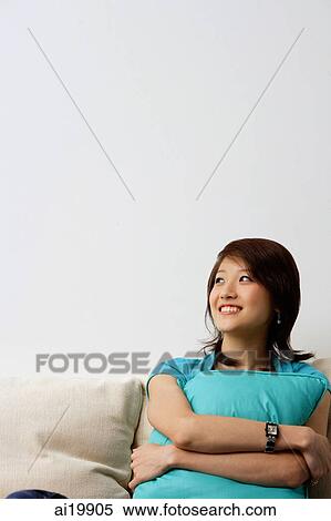 Woman sitting on sofa, hugging cushion, looking away View Large Photo Image Stock Photography - Woman sitting on sofa, hugging cushion, looking away. Fotosearch