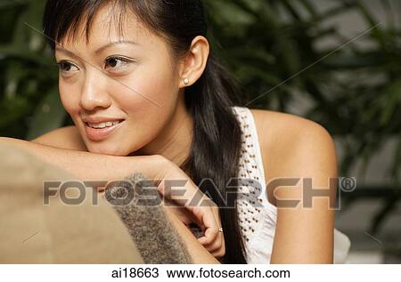Stock Image - Woman sitting on sofa, leaning chin on arm, looking away. Fotosearch