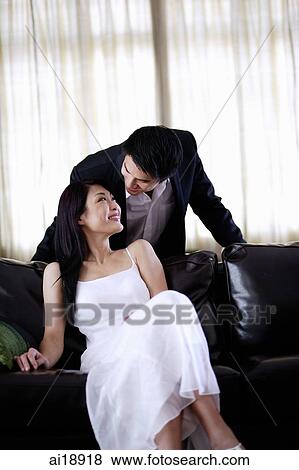 Stock Photo - Woman sitting on sofa, man behind her, leaning forward. Fotosearch