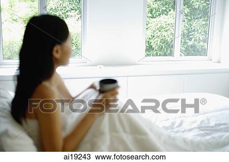 Woman sitting up in bed, holding cup, looking away View Large Photo Image Stock Image - Woman sitting up in bed, holding cup, looking away. Fotosearch