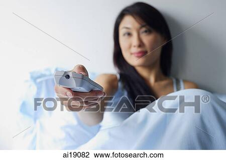 Woman sitting up in bed, holding TV remote control View Large Photo Image Stock Image - Woman sitting up in bed, holding TV remote control. Fotosearch