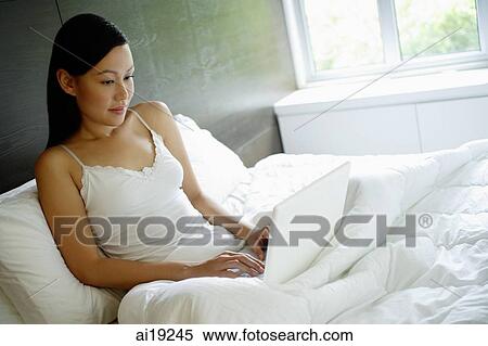 Woman sitting up in bed, using laptop View Large Photo Image Stock Photography - Woman sitting up in bed, using laptop. Fotosearch