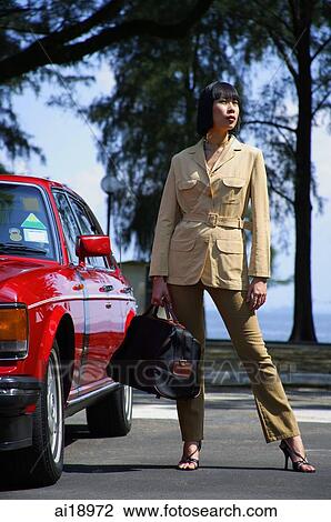 Woman standing by red car, carrying bag, looking away, outdoor location View Large Photo Image Stock Image - Woman standing by red car, carrying bag, looking away, outdoor location. Fotosearch