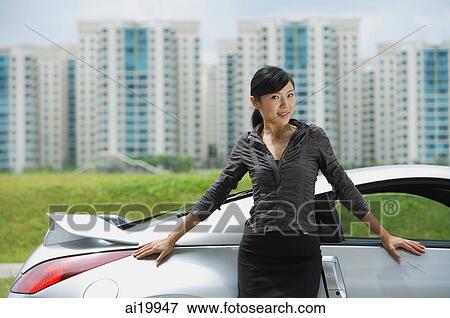 Woman standing next to silver sports car, looking at camera, smiling View Large Photo Image Stock Photo - Woman standing next to silver sports car, looking at camera, smiling. Fotosearch