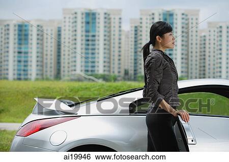 Woman standing next to silver sports car, looking away View Large Photo Image Stock Photograph - Woman standing next to silver sports car, looking away. Fotosearch