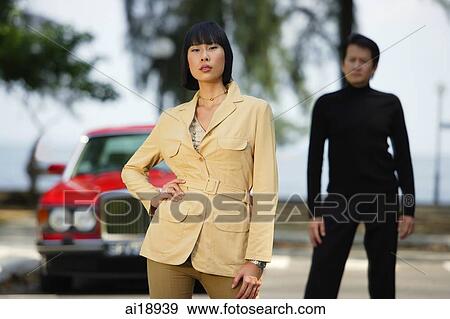 Woman standing with hand on hip, man in the background View Large Photo Image Stock Photo - Woman standing with hand on hip, man in the background. Fotosearch