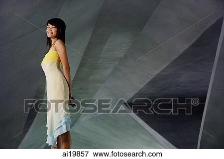 Stock Photo - Woman standing with hands behind her back, smiling. Fotosearch
