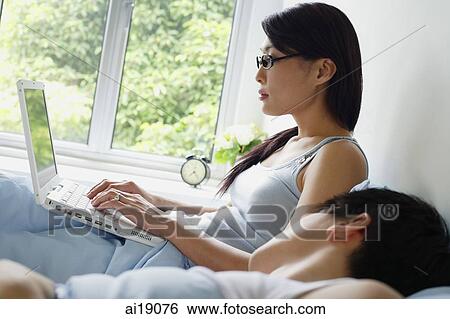 Woman using laptop in bed, man sleeping next to her View Large Photo Image Stock Photograph - Woman using laptop in bed, man sleeping next to her. Fotosearch