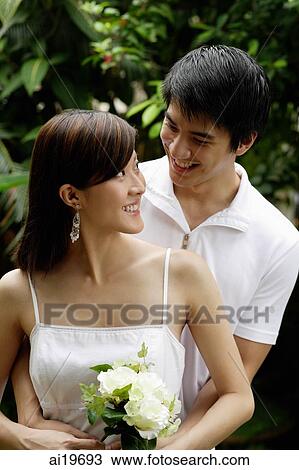 Stock Image - Woman with bouquet of flowers turning to look at man standing behind her. Fotosearch