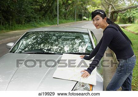 Stock Photo - Woman with map, standing next to car, looking at camera. Fotosearch