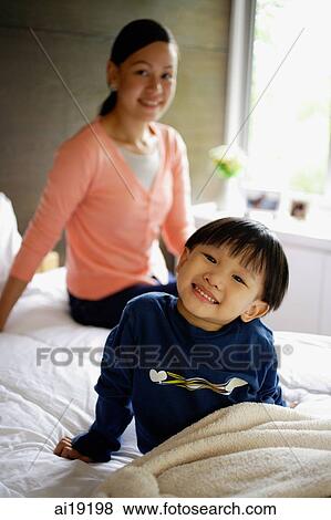 Young boy sitting on bed, smiling at camera, mother in the background View Large Photo Image Stock Photo - Young boy sitting on bed, smiling at camera, mother in the background. Fotosearch