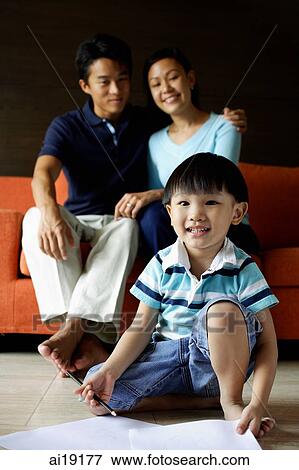 Stock Photo - Young boy sitting on floor, parents in background sitting on sofa. Fotosearch