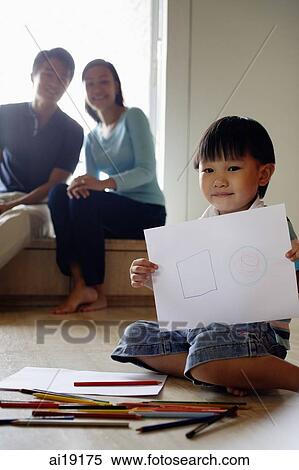 Stock Photography - Young boy sitting on floor with drawing paper and coloured pencils, people in the background. Fotosearch