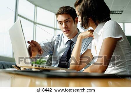 Stock Image - Young executives sitting side by side, working with laptop. Fotosearch