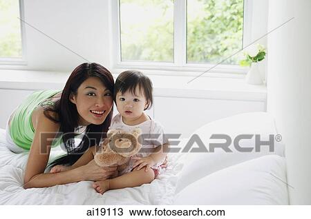 Young girl sitting on bed, mother leaning next to her, smiling at camera View Large Photo Image Stock Image - Young girl sitting on bed, mother leaning next to her, smiling at camera. Fotosearch