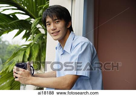 Young man holding mug, smiling at camera View Large Photo Image Stock Photo - Young man holding mug, smiling at camera. Fotosearch