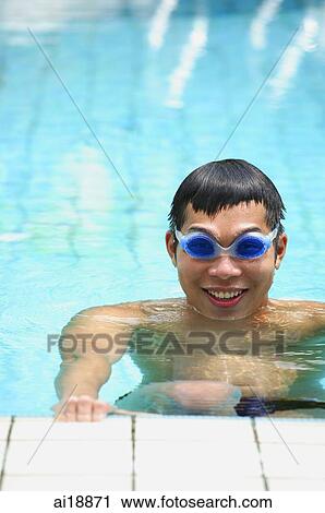 Stock Image - Young man in swimming pool, wearing goggles, smiling at camera. Fotosearch