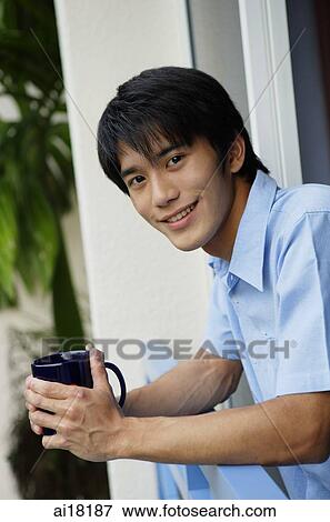Stock Photo - Young man leaning on railing, holding mug, smiling at camera. Fotosearch