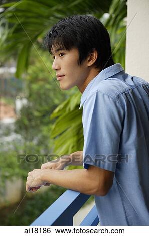 Stock Photograph - Young man leaning on railing, looking away. Fotosearch