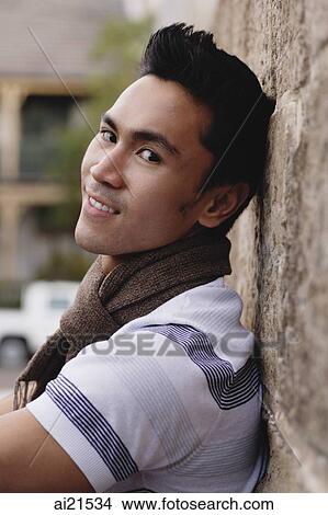 Young man leaning on wall, smiling at camera View Large Photo Image Picture - Young man leaning on wall, smiling at camera. Fotosearch