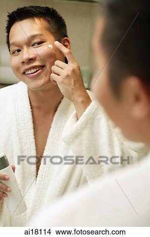 Young man looking in mirror, applying moisturizer View Large Photo Image Picture - Young man looking in mirror, applying moisturizer. Fotosearch