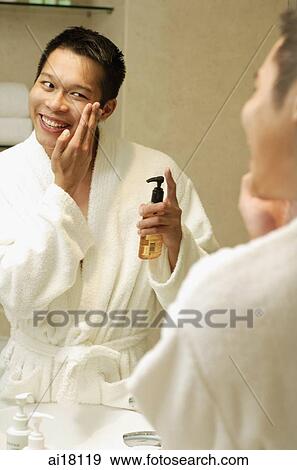 Young man looking in mirror, applying lotion to face View Large Photo Image Stock Photo - Young man looking in mirror, applying lotion to face. Fotosearch