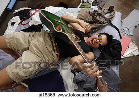Young man lying messy bed, playing guitar View Large Photo Image Stock Photo - Young man lying messy bed, playing guitar. Fotosearch