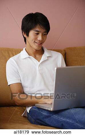 Young man on sofa, using laptop View Large Photo Image Stock Photo - Young man on sofa, using laptop. Fotosearch
