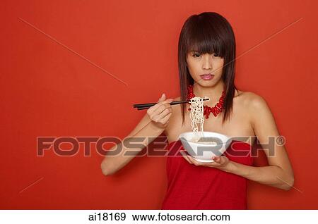 Stock Photo - Young woman holding bowl of noodles, looking at camera. Fotosearch