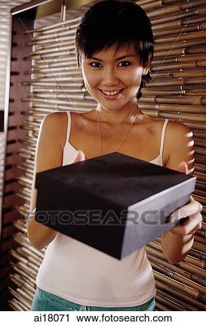 Young woman holding box, looking at camera View Large Photo Image Stock Image - Young woman holding box, looking at camera. Fotosearch