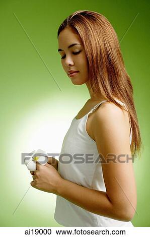 Stock Image - Young woman holding Frangipani flower, eyes closed. Fotosearch