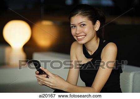 Stock Photo - Young woman holding mobile phone, looking at camera. Fotosearch