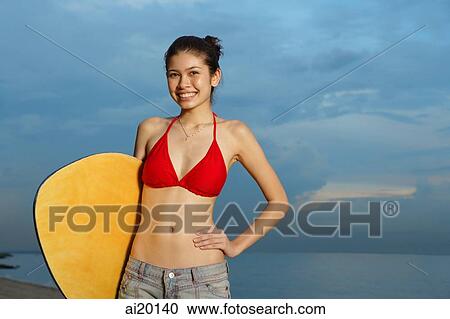 Young woman holding skimboard, hand on hip View Large Photo Image Stock Image - Young woman holding skimboard, hand on hip. Fotosearch