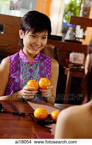 Young woman holding two oranges, smiling at person in front of her View Large Photo Image Picture - Young woman holding two oranges, smiling at person in front of her. Fotosearch