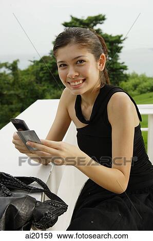 Young woman in black dress, holding mobile phone and credit card, smiling at camera View Large Photo Image Stock Photo - Young woman in black dress, holding mobile phone and credit card, smiling at camera. Fotosearch
