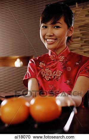 Young woman in Chinese dress holding a tray with two oranges, smiling at camera View Large Photo Image Stock Image - Young woman in Chinese dress holding a tray with two oranges, smiling at camera. Fotosearch