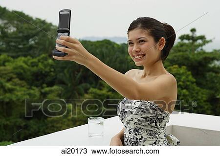 Young woman in floral dress, standing on balcony, using mobile phone to take a picture View Large Photo Image Stock Image - Young woman in floral dress, standing on balcony, using mobile phone to take a picture. Fotosearch