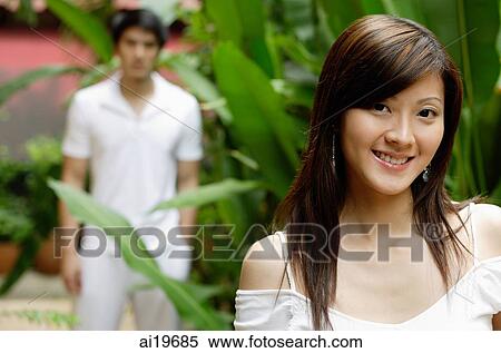 Young woman in garden, smiling at camera, man in the background View Large Photo Image Stock Photography - Young woman in garden, smiling at camera, man in the background. Fotosearch