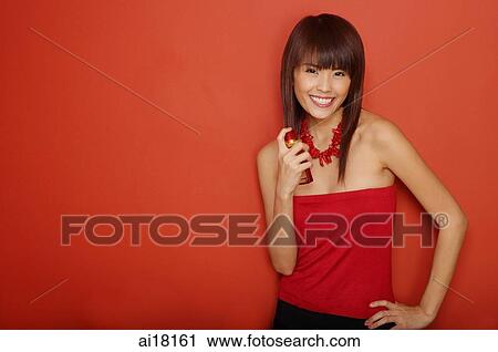 Stock Image - Young woman in red tube top applying perfume. Fotosearch