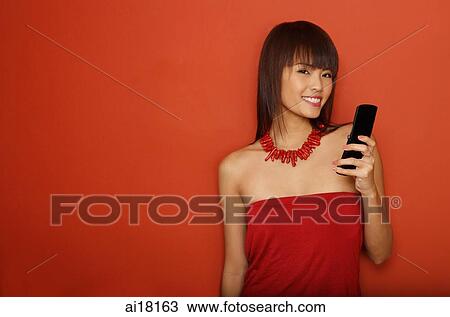 Stock Image - Young woman in red tube top with mobile phone. Fotosearch