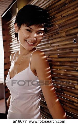 Young woman leaning on bamboo screen, smiling View Large Photo Image Stock Photo - Young woman leaning on bamboo screen, smiling. Fotosearch