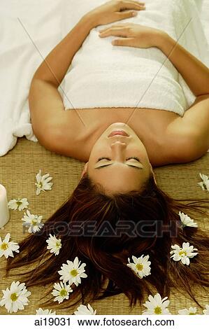 Stock Image - Young woman lying on back, flowers scattered around her. Fotosearch